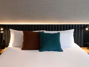 A neatly made bed with white sheets, two pillows (one brown and one teal), and a black headboard with a textured design. - Novotel Sydney City Centre (Sydney)