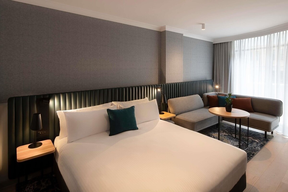A hotel room with a large bed, a sofa, a small table, and a lamp.