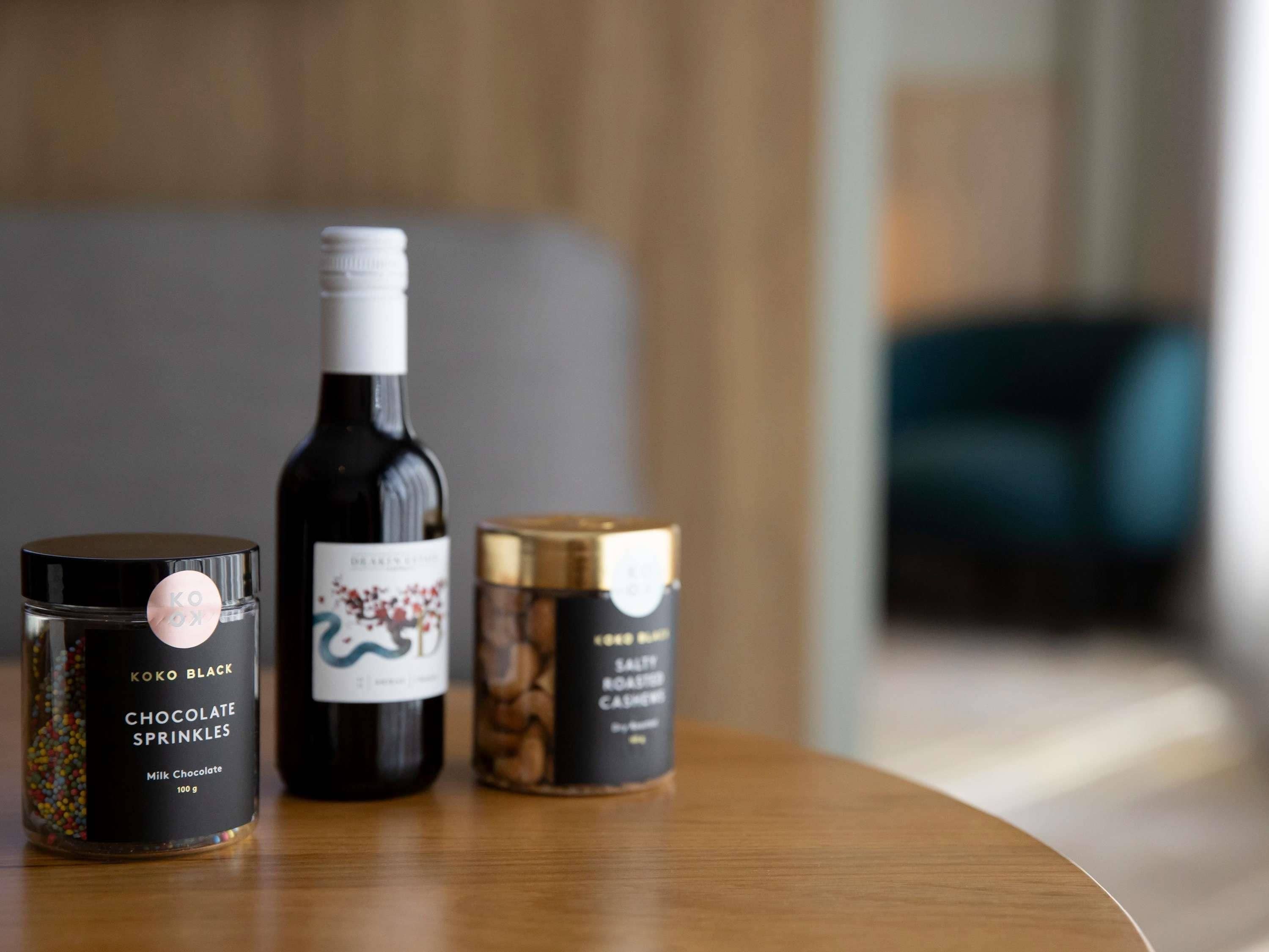 Tres objetos sobre una mesa de madera: una botella de chocolate con trocitos, una botella de vino y un recipiente con granos de café.