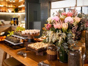 A buffet table with various food items and a floral centerpiece. - Novotel Sydney City Centre (Sydney)