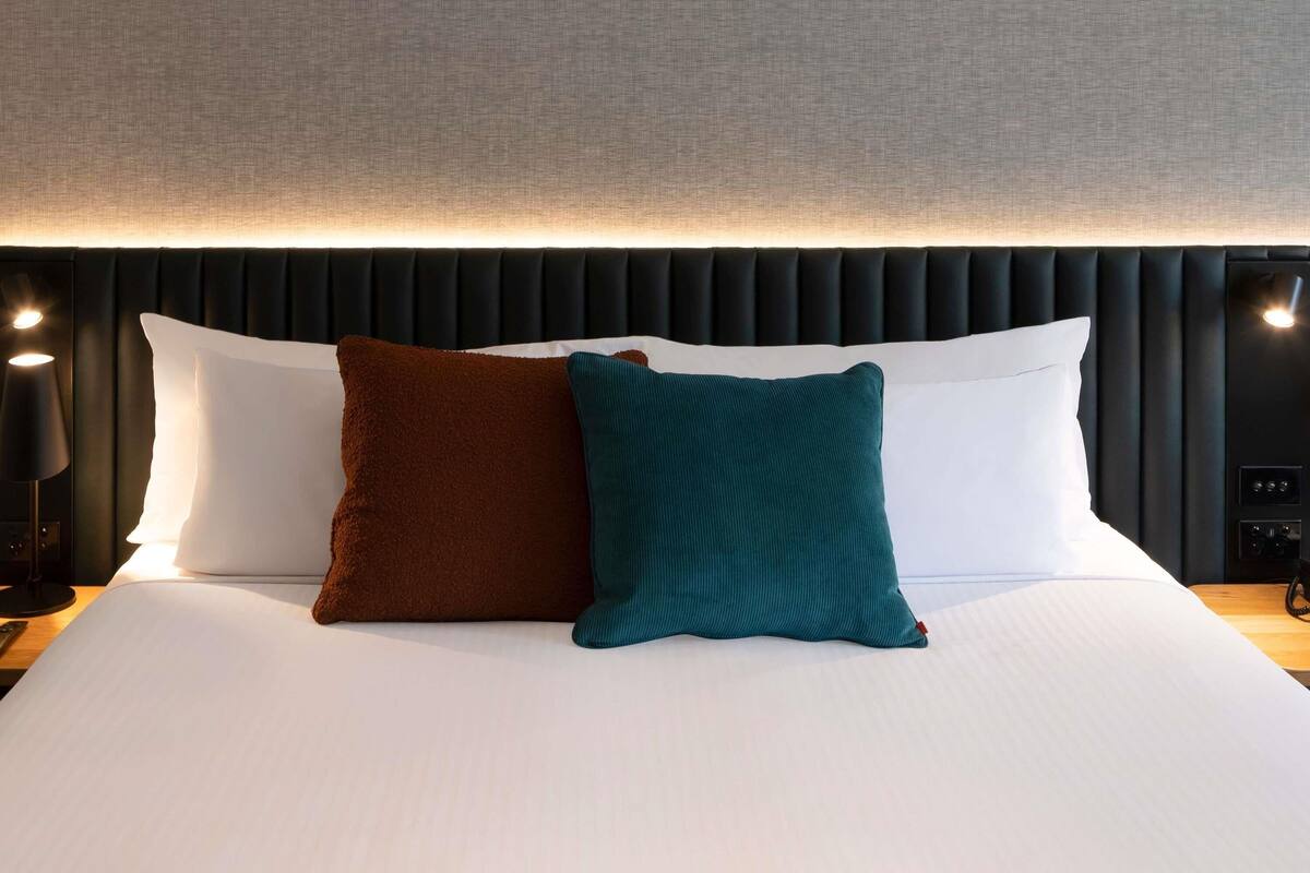 A neatly made bed with white sheets, two pillows (one brown and one teal), and a black headboard with a textured design.
