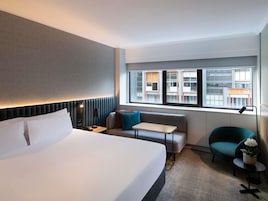 Habitación de hotel con cama, escritorio, silla y ventana con vista a edificios.