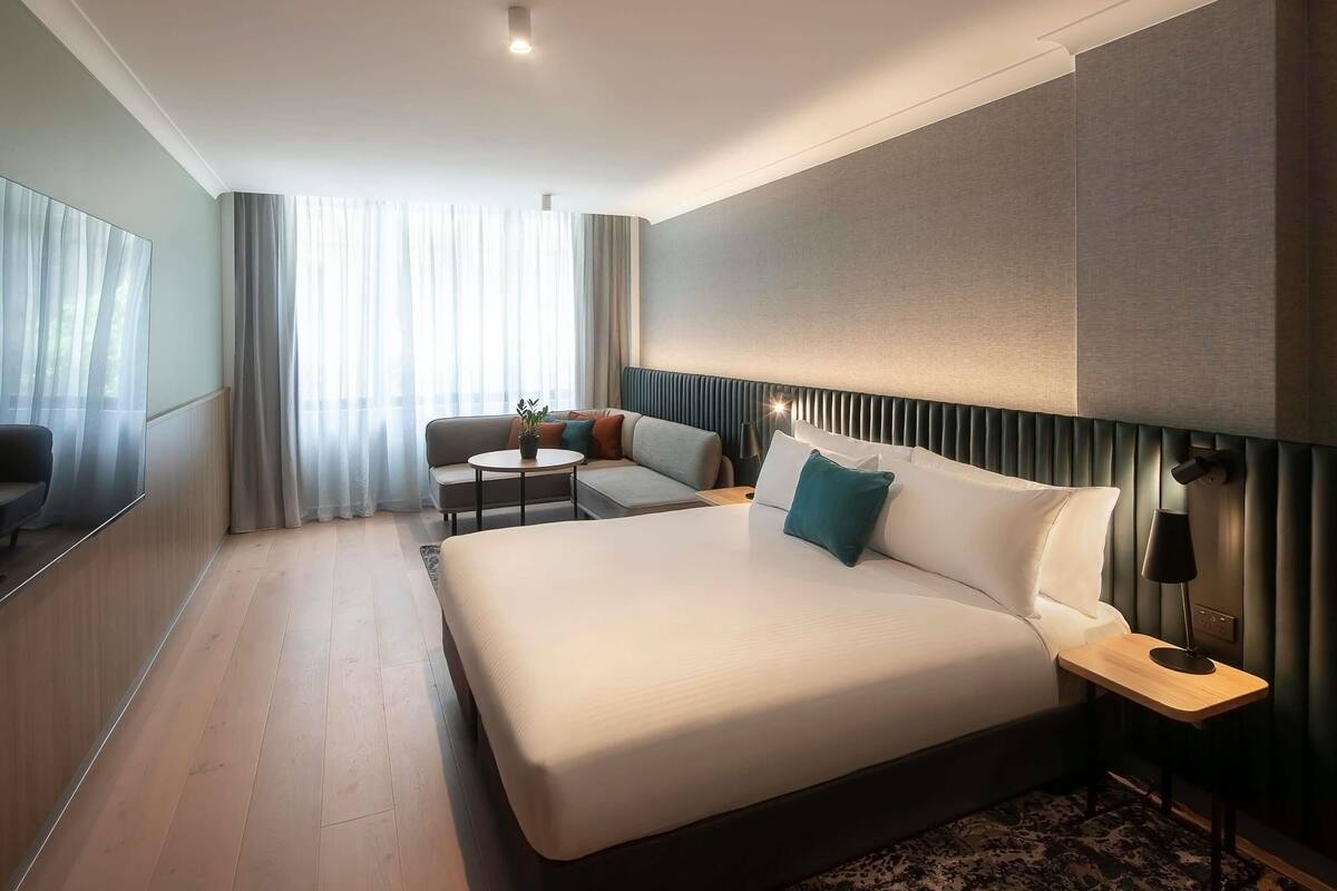 A modern hotel room with a large bed, a sofa, a small table, and a TV.