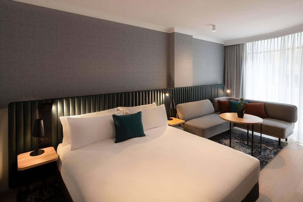 A hotel room with a large bed, a sofa, a small table, and a lamp.