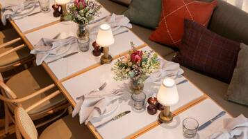 Mesa de jantar posta com toalhas brancas, pratos, talheres, copos e centros de mesa com flores.