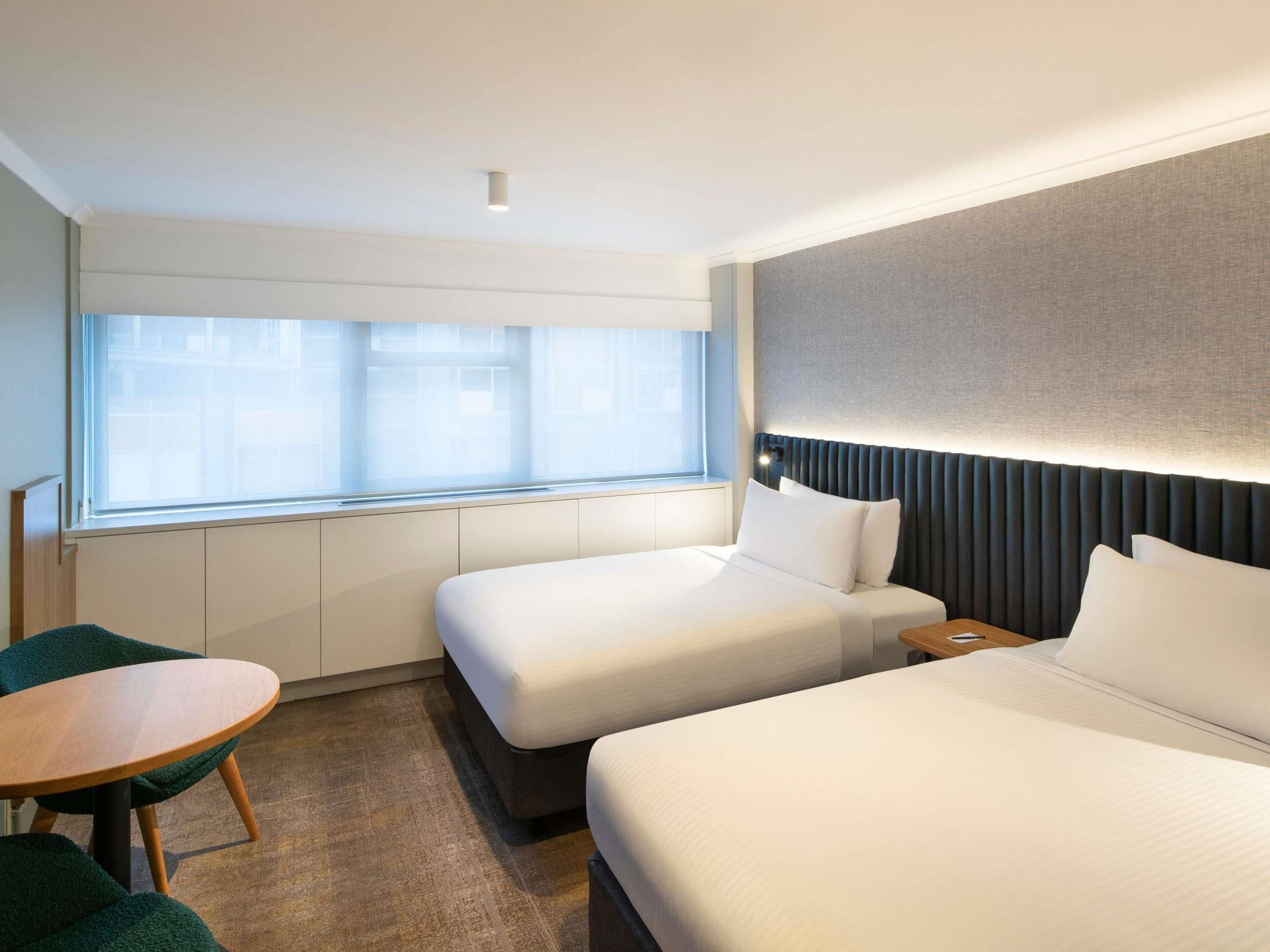 Habitación de hotel con dos camas, una mesita y una ventana con persianas.