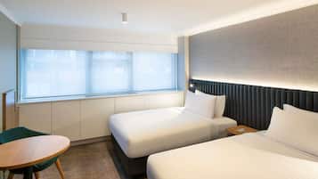 Habitación de hotel con dos camas, una mesita y una ventana con persianas.