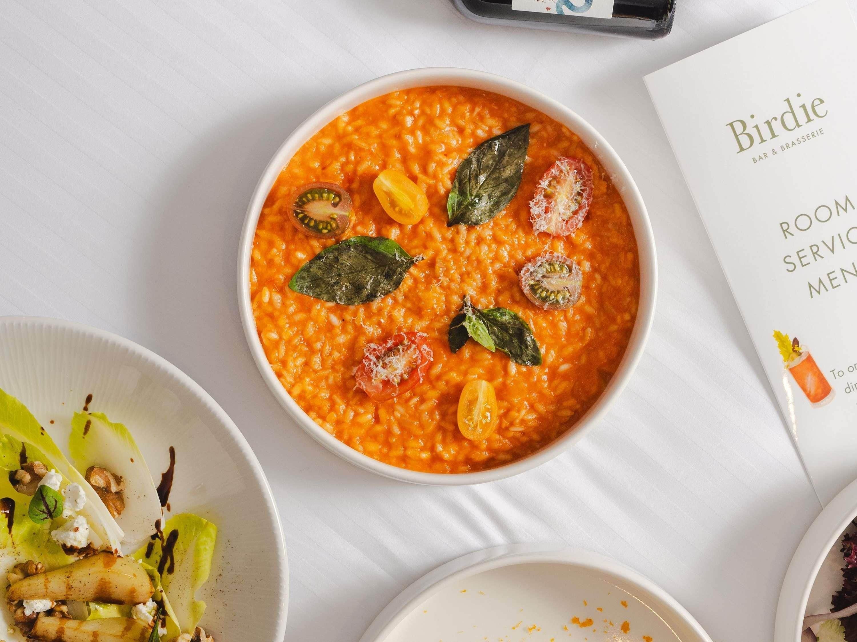 A bowl of soup garnished with basil and cherry tomatoes, a menu, and a plate with a salad.