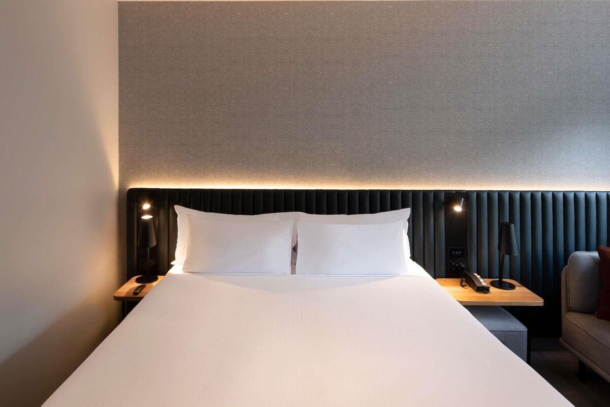A hotel room with a large bed, bedside tables, a desk, and a chair.