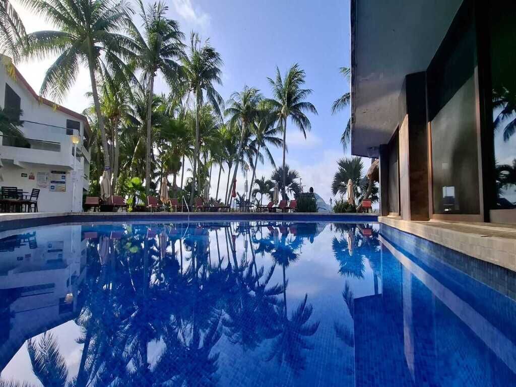 A swimming pool with reflections of palm trees, surrounded by lounge chairs and a building facade.