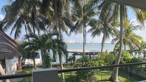 A balcony with a table and chairs, overlooking a beach with palm trees and a view of the city skyline. - Sina Suites Cancún - Adults Only (Cancun)