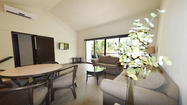 A modern living room with a dining area, a sofa, a coffee table, and a large window with a view of greenery. - Sina Suites Cancún - Adults Only (Cancun)