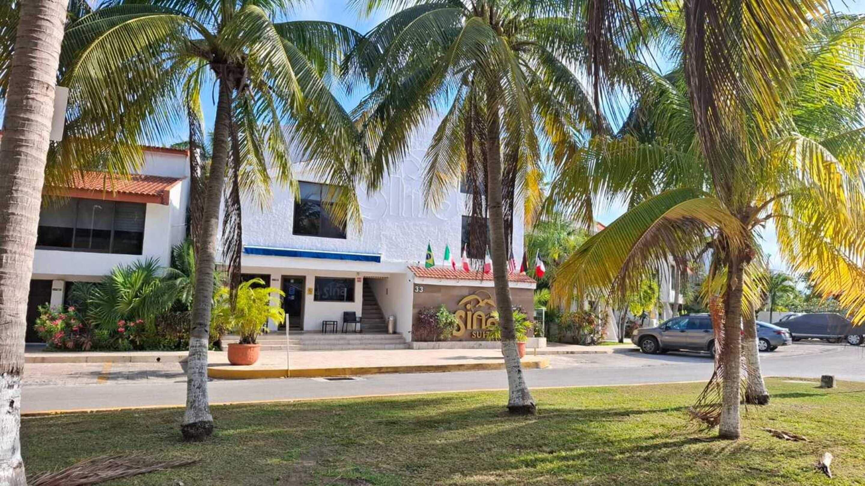 Un hotel con fachada blanca, palmeras y un cartel que dice 'Sina Suites'.