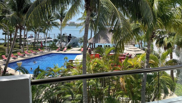 A pool area with lounge chairs and palm trees, overlooking a body of water. - Sina Suites Cancún - Adults Only (Cancun)