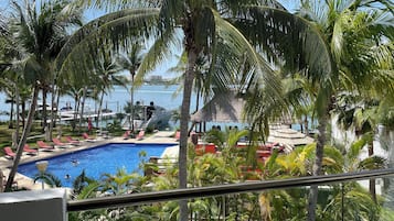 A pool area with lounge chairs and palm trees, overlooking a body of water.