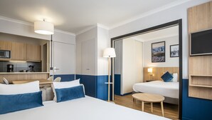 A hotel room with a large bed, a small table, a desk with a chair, a kitchenette, and a bathroom visible through an open door. - Aparthotel Adagio La Defense Kleber (Courbevoie)