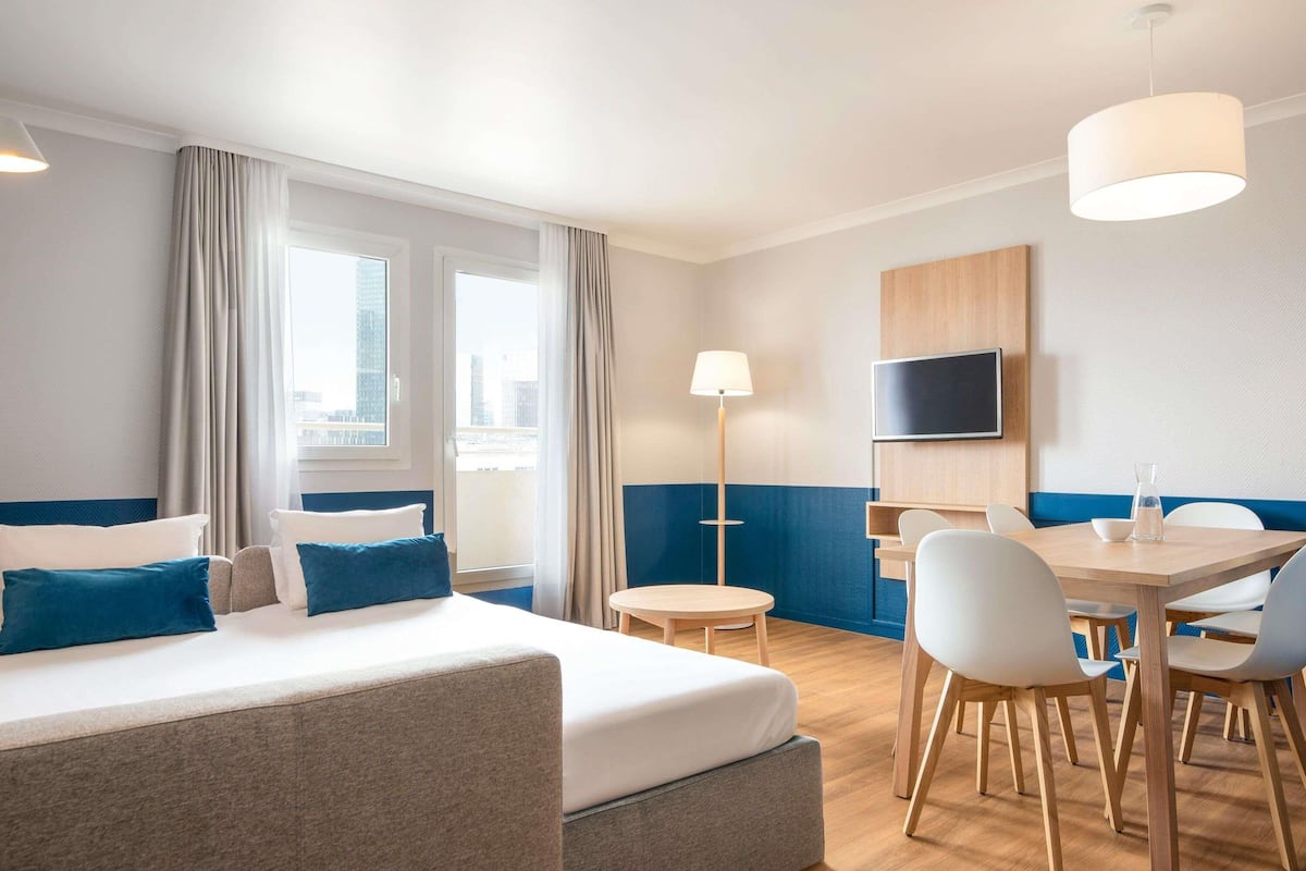 A hotel room with a bed, a desk, chairs, a TV, and a lamp.