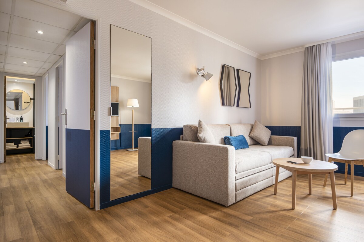 A modern hotel room with a sofa, a small round table, and a mirror.