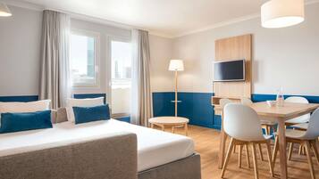 A hotel room with a bed, a desk, chairs, a TV, and a lamp.