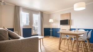 A modern hotel room with a sofa, dining table, chairs, a TV, and a large window with curtains. - Aparthotel Adagio La Defense Kleber (Courbevoie)