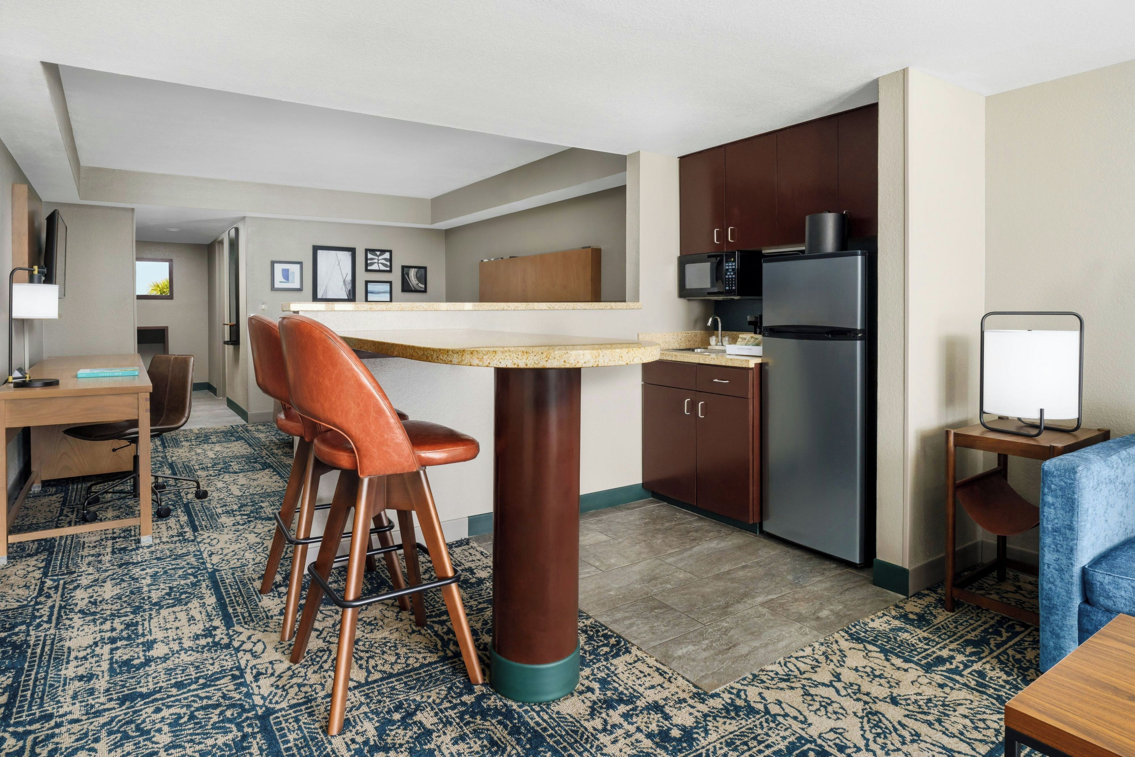 A compact hotel room with a kitchenette, a dining area, and a seating space.