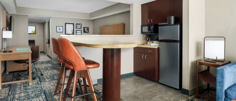 A compact hotel room with a kitchenette, a dining area, and a seating space.