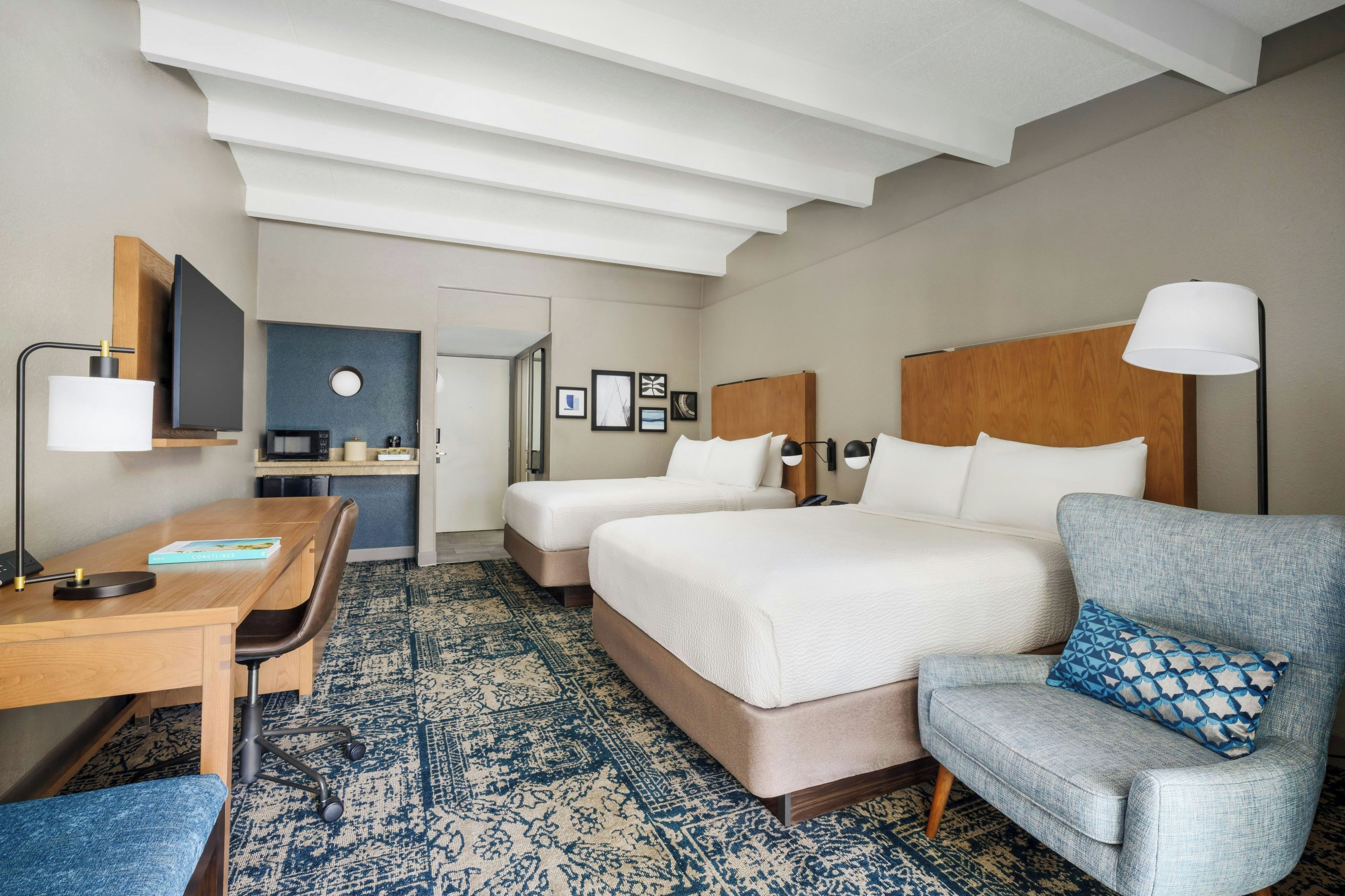 A hotel room with a bed, a desk, a chair, a lamp, and a television.