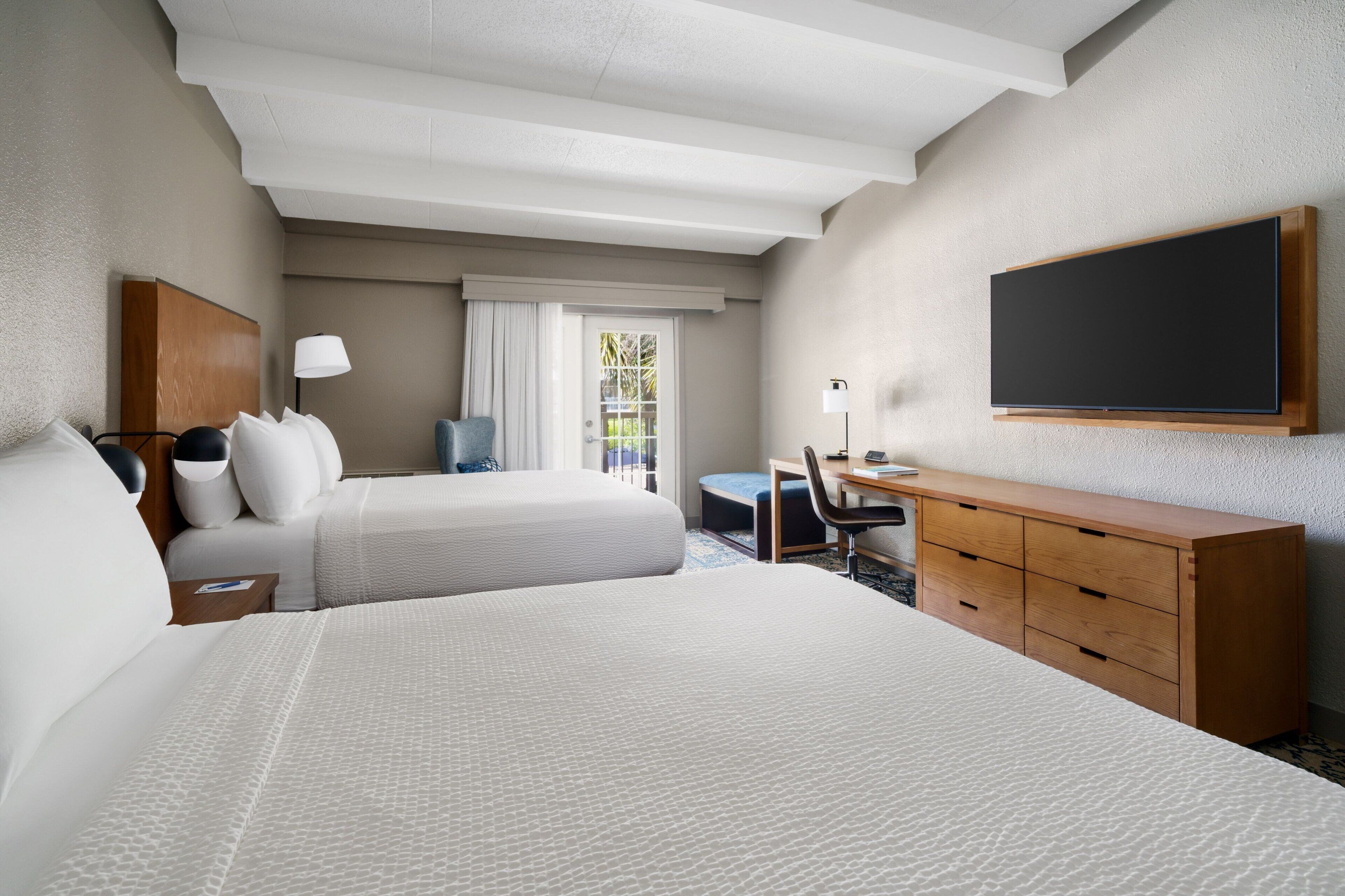 Ein Hotelzimmer mit zwei Betten, einem Schreibtisch, einem Stuhl, einem Fernseher und einem Kleiderschrank.