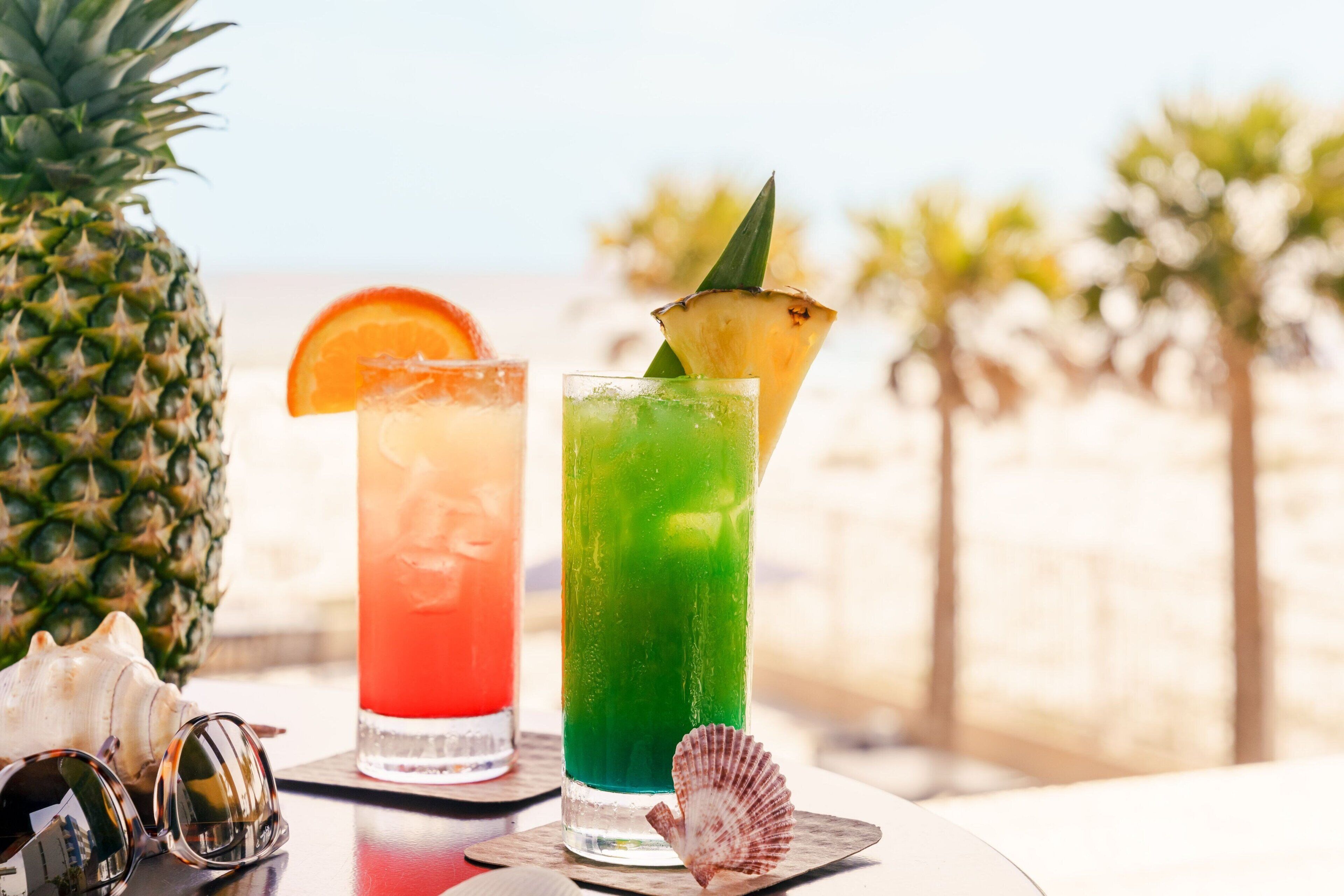 Two cocktails on a table with a pineapple and a shell, suggesting a tropical setting.
