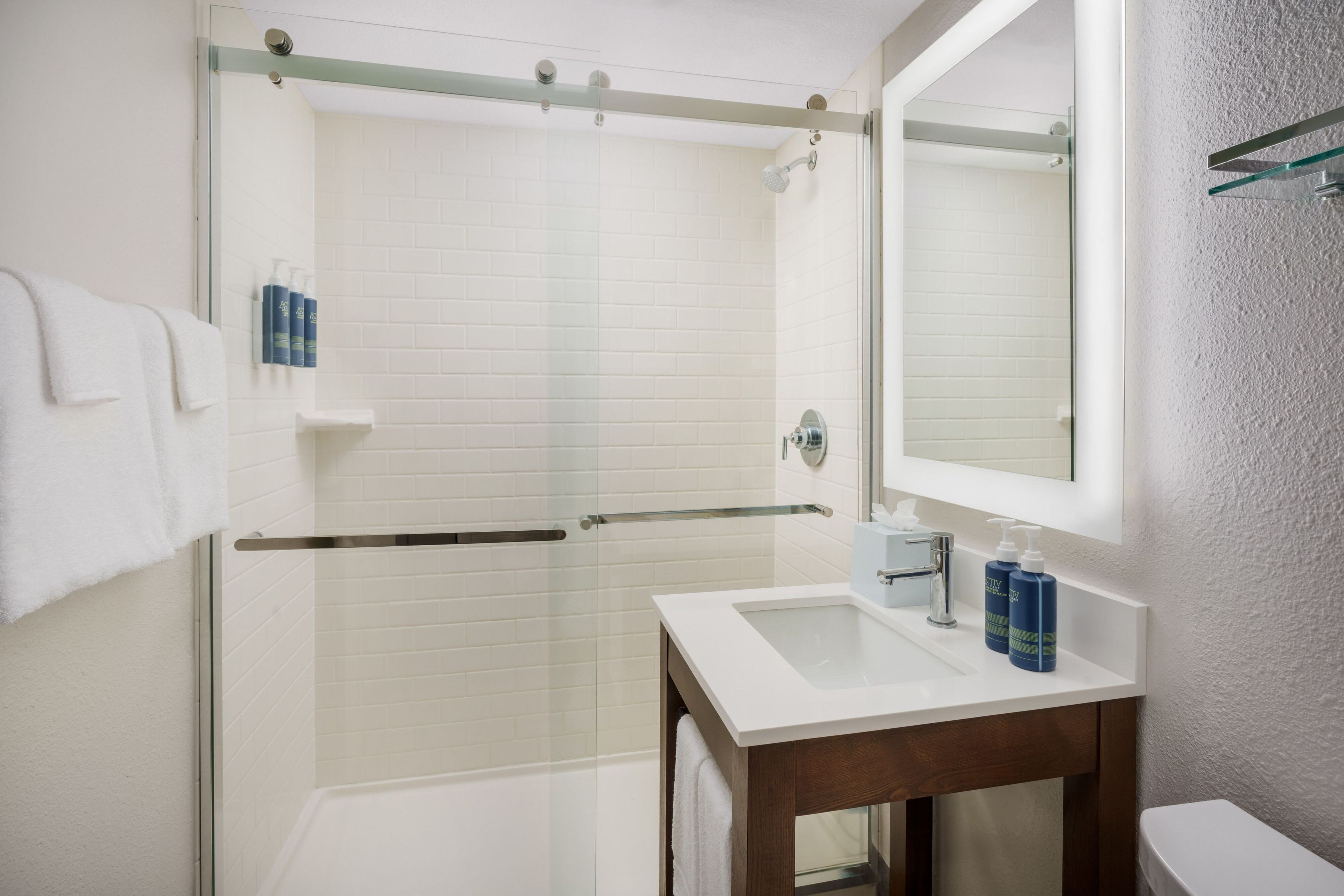 A modern bathroom with a glass shower enclosure, a white sink with a mirror, and a wooden vanity.