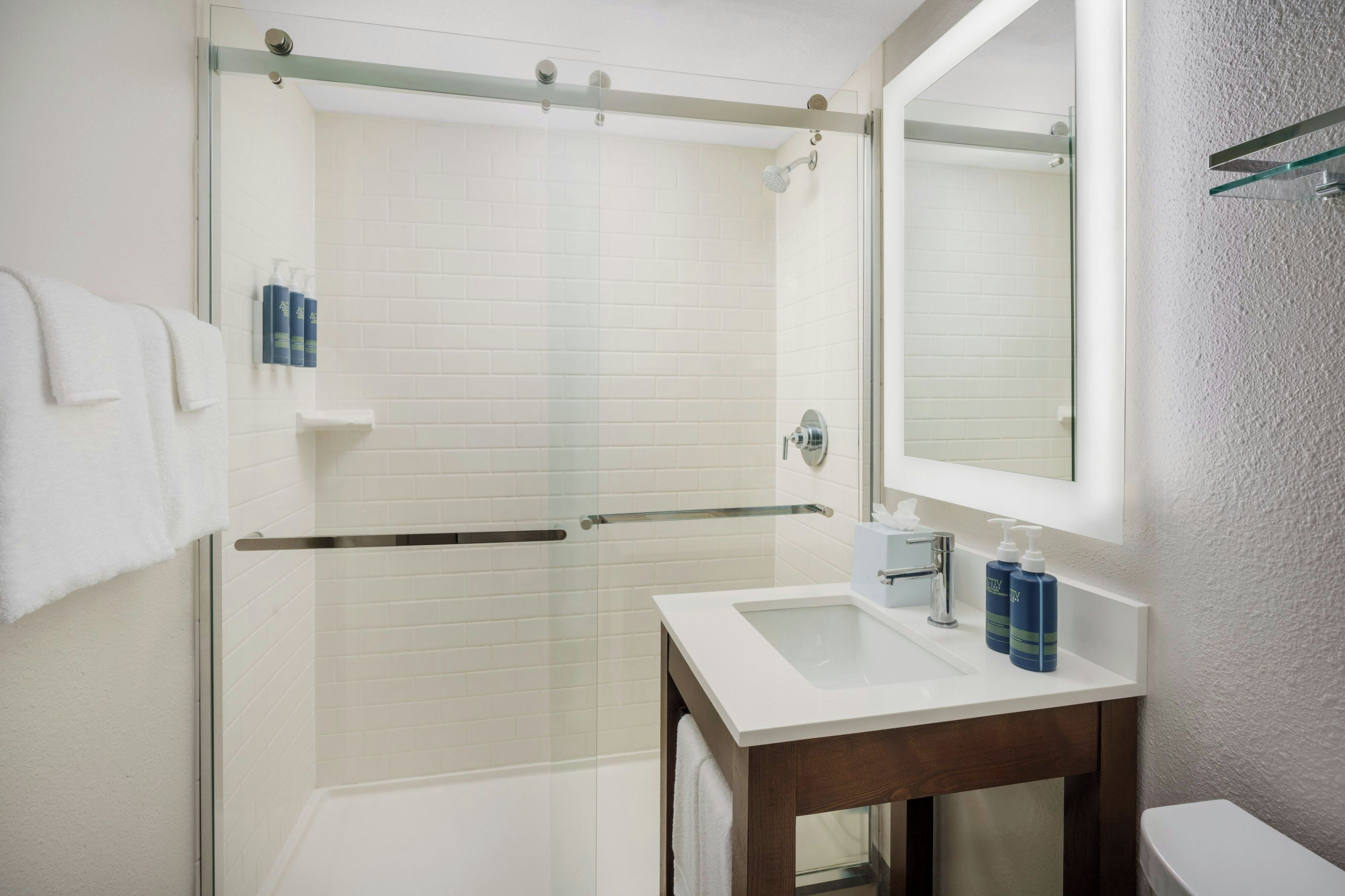 A modern bathroom with a glass shower enclosure, a white sink with a mirror, and toiletries on the wall.