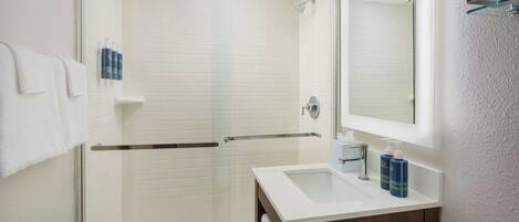 A modern bathroom with a glass shower enclosure, a white sink with a mirror, and toiletries on the wall.