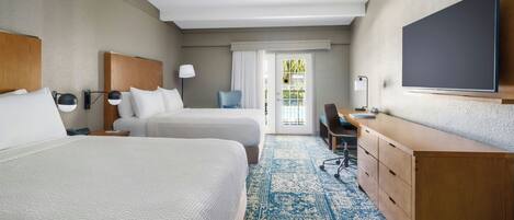A hotel room with two beds, a desk, a chair, a TV, and a view of the outside.