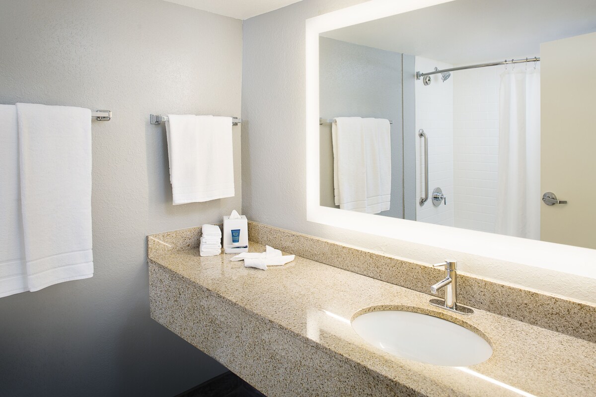 A modern bathroom with a granite countertop, a sink, a large mirror, and two towels hanging on the wall.