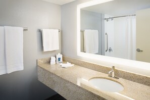 A modern bathroom with a granite countertop, a sink, a large mirror, and two towels hanging on the wall. - Four Points by Sheraton Destin-Fort Walton Beach (Fort Walton Beach)