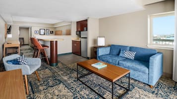 A modern living room with a blue sofa, a wooden coffee table, a patterned rug, and a view of the city through a window.