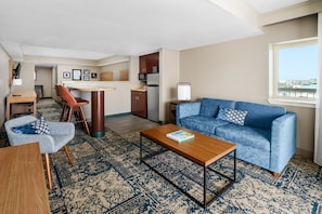 A modern living room with a blue sofa, a wooden coffee table, a patterned rug, and a view of the city through a window.