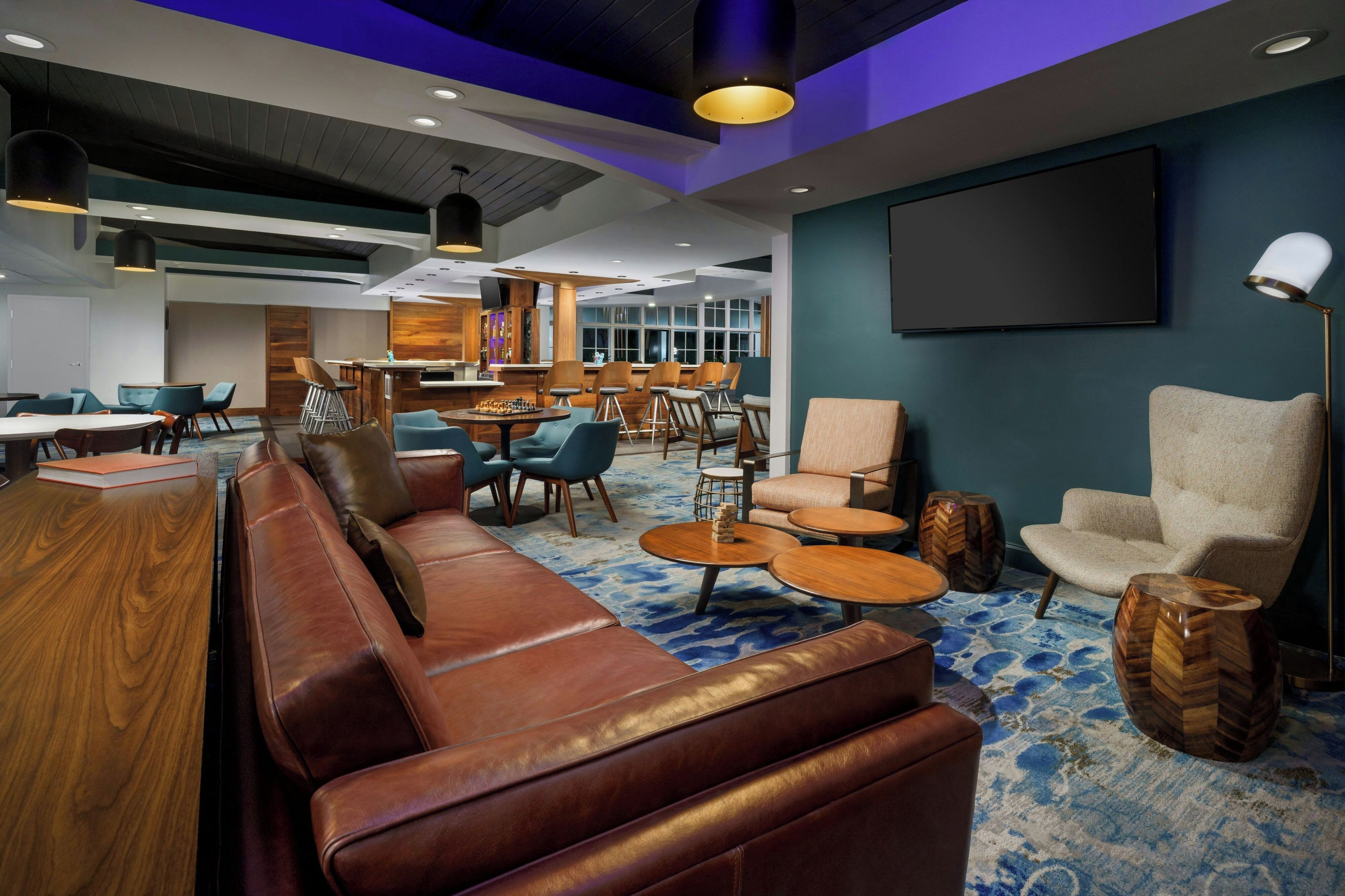 Un área de lounge moderna con sofás de cuero, un bar y una pared con pantalla grande.