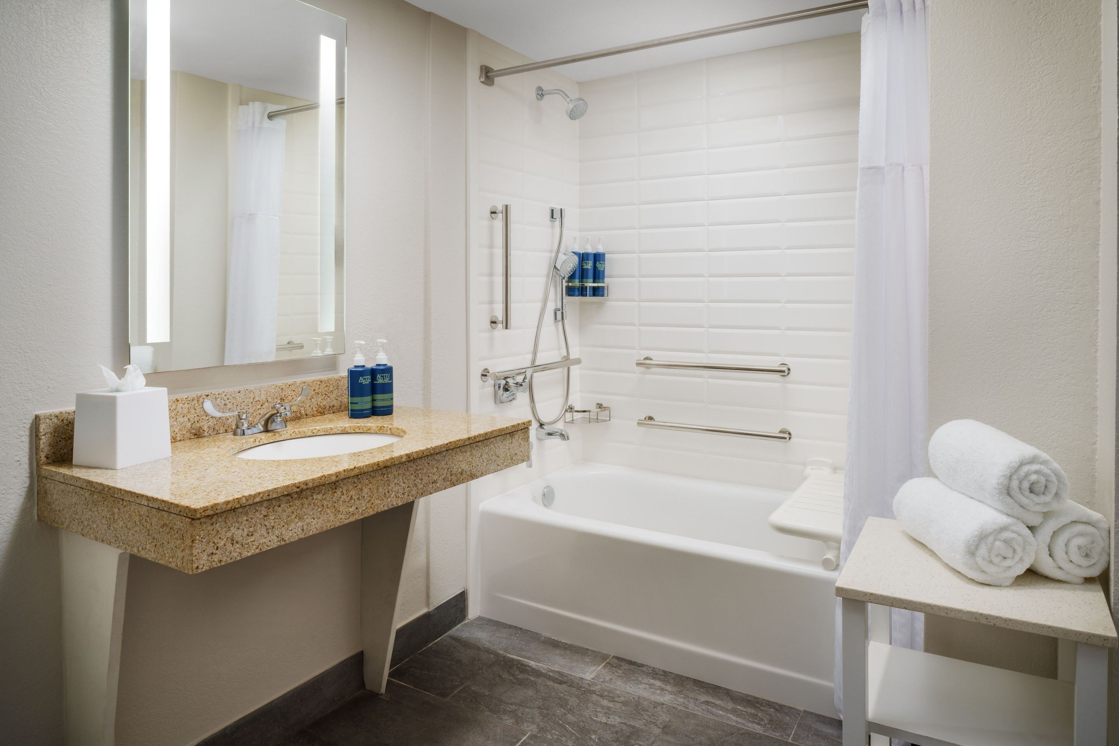 A bathroom with a sink, mirror, shower, and a shelf with towels.