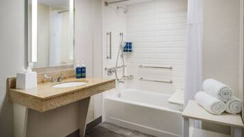 A bathroom with a sink, mirror, shower, and a shelf with towels.
