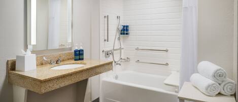 A bathroom with a sink, mirror, shower, and a shelf with towels.