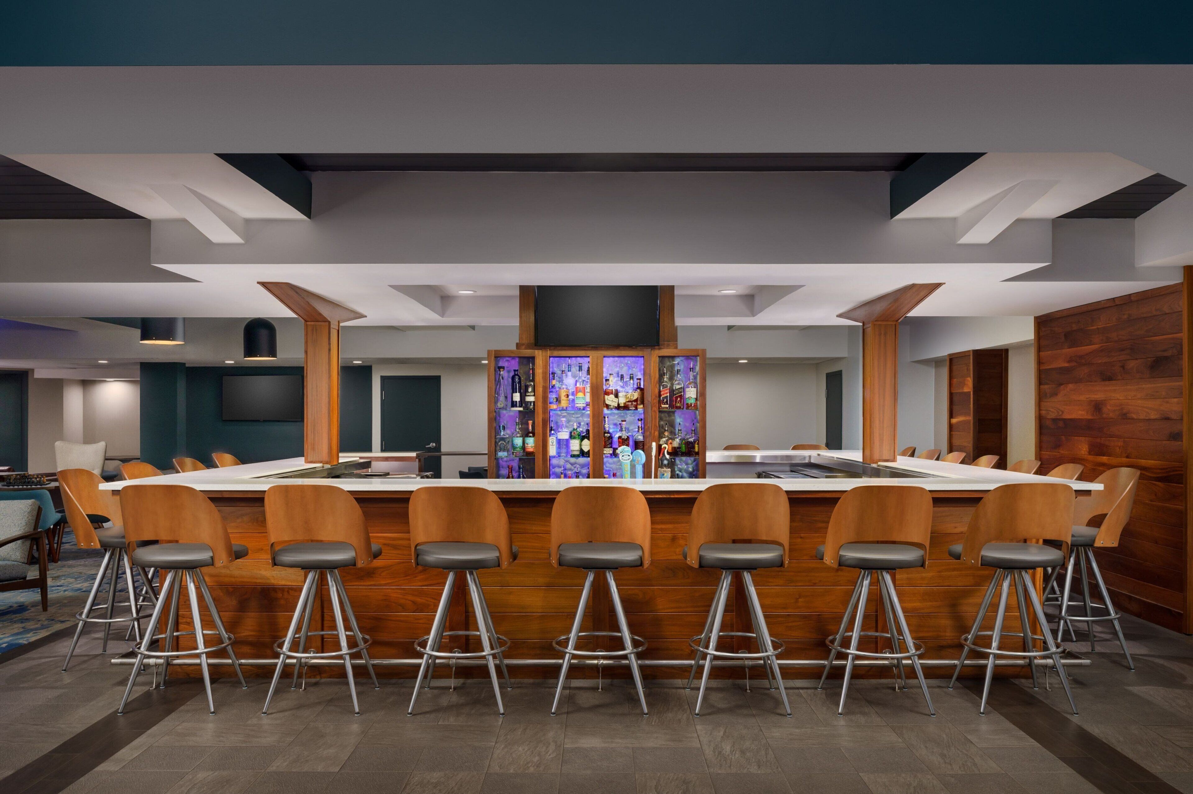 Una sala de conferencias moderna con una larga mesa, taburetes altos y una zona de bar con botellas.