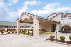 A hotel entrance with a covered parking area, a handicap parking sign, and a building with multiple windows and a balcony.