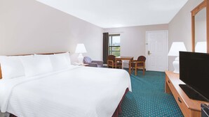 Habitación de hotel con una cama grande, un escritorio con silla, televisor y ventana con cortinas.