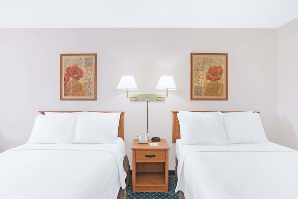 A hotel room with two beds, a nightstand with a lamp, and two framed floral artworks on the wall.