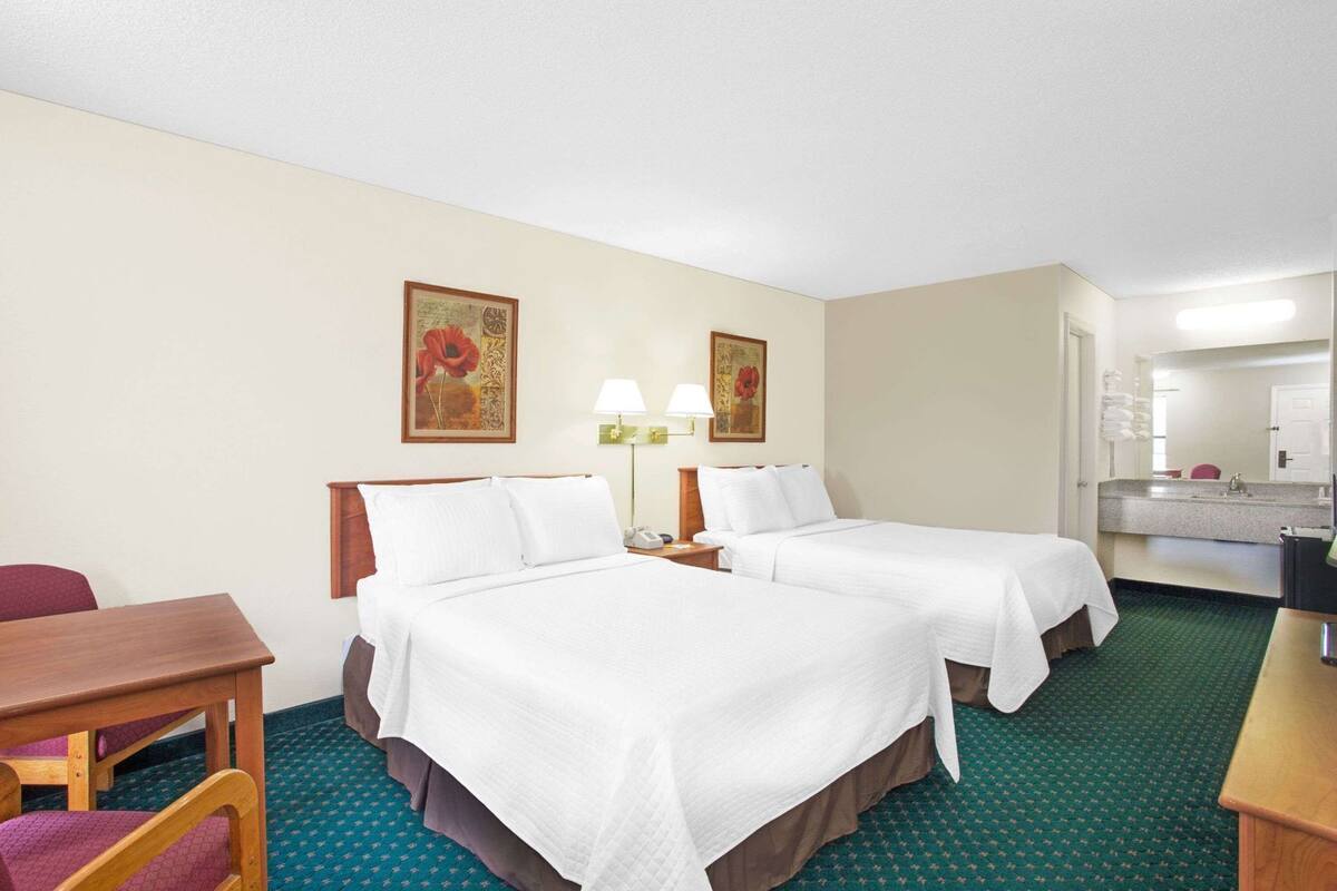 A hotel room with two beds, a desk, a chair, a lamp, and a mirror.
