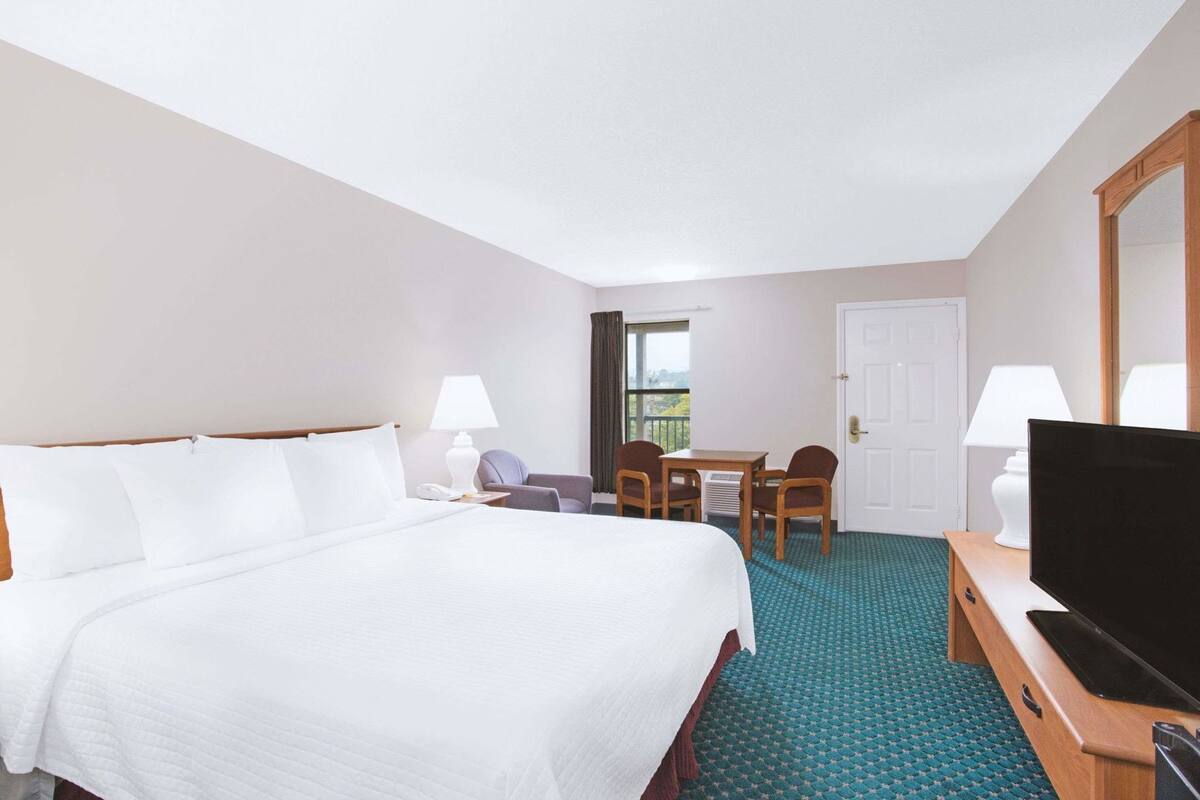 A hotel room with a large bed, a desk with two chairs, a television, and a door leading to a balcony.