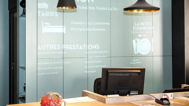A hotel reception desk with a computer, a telephone, and a glass display case. - ibis Toulon La Seyne Sur Mer (La Seyne-sur-Mer)