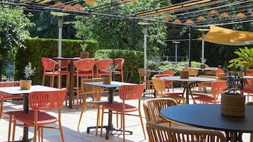 An outdoor patio area with tables and chairs, surrounded by greenery.