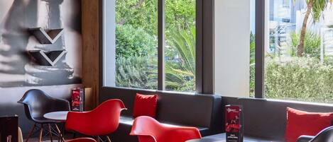 A modern dining area with red chairs, black tables, and a view of greenery outside.